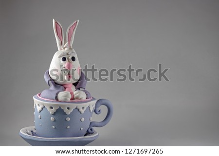 Alice in Wonderland, marzipan rabbit, bunny in the cup with saucer on the gray background, cake decoration