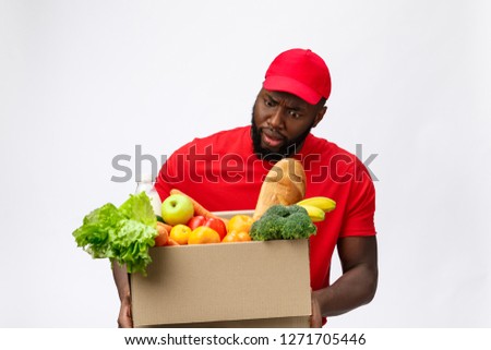Young african american man holding grocery box in hands with shocking face. Isolated over Grey background.