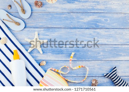 Creative flat lay concept of summer travel vacations. Top view of beach towel sunscreen bottle swimwear seashells starfish on pastel blue wooden planks background with copy space mockup template text