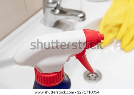 Blue cleaning spray bottle close up with yellow rubber gloves on background.