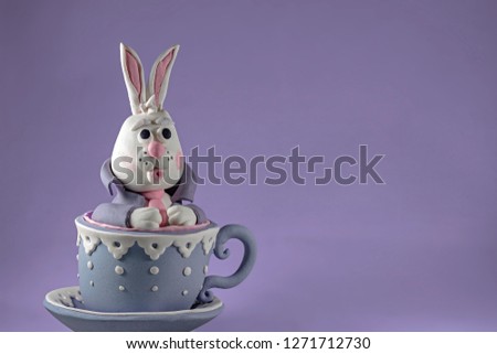Alice in Wonderland, marzipan rabbit, bunny in the cup with saucer on the gray background, cake decoration
