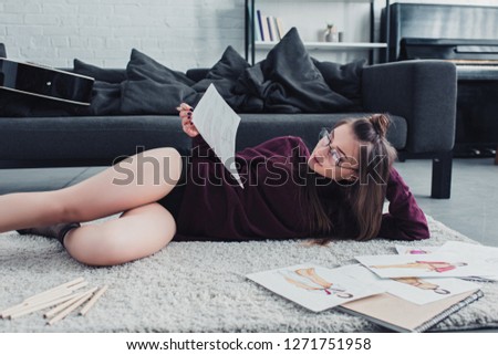 attractive designer lying on carpet near sofa and holding sketch in living room