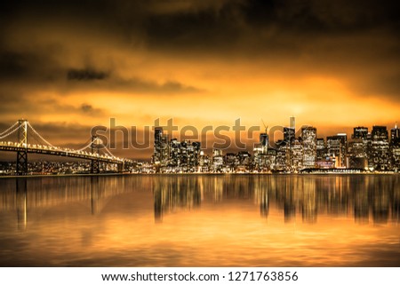 View of San Francisco skyline under golden sunset sky with lights and Bay Bridge
