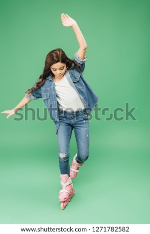child in denim rollerblading with outstretched hands on green background