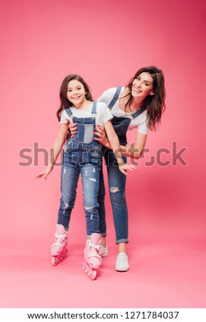 smiling mother teaching daughter roller on pink background