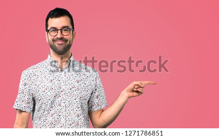 Handsome man with glasses pointing to the lateral on pink background