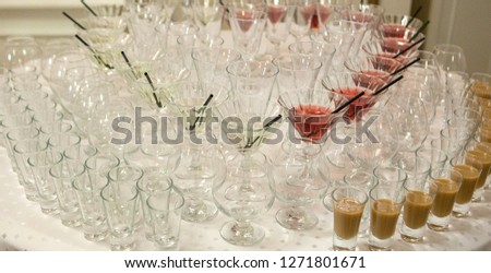 Beautiful row line of different colored alcohol cocktails on a party, martini, vodka,and others on decorated catering bouquet table on open air event, picture with beautiful bokeh.
