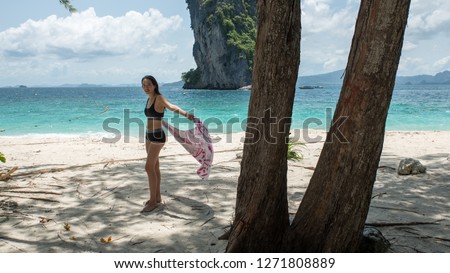 Young woman standing on tropical beach holding towel and islandn in background
