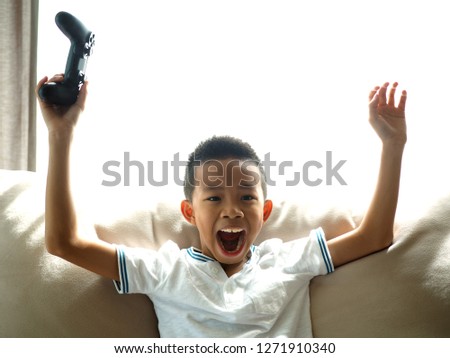 Asian boy holding a game controller and raising his arms up in the air.