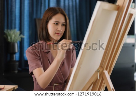 A beautiful Asian artist in a pink dress begins to use the brush to draw and create beautiful works of art.