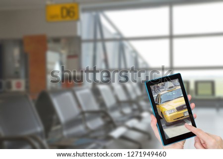 Hands of tourist touching tablet screen with a yellow taxi cab. Intentionally blurred image of a empty airport inside terminal is in the background. All potential trademarks are removed.