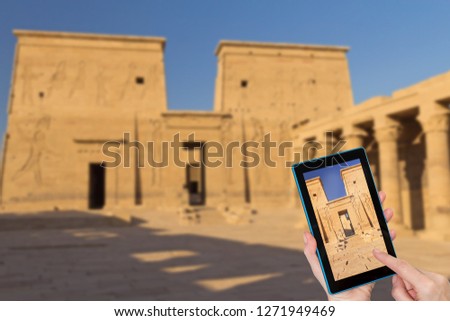 Hands of tourist touching tablet screen with a focused entrance to the Philae Temple. Intentionally blurred image of Philae Temple  is in the background. (Egypt )