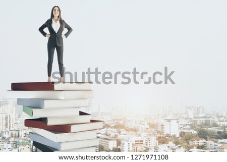 Attractive young businesswoman standing on pile of books on city background. Success and education concept 