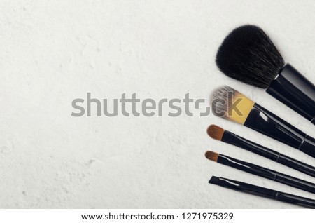 Black makeup brushes on a light stone background. Professional tools for make-up artist. Flat Lay, top view, copy space.