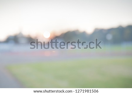 BLURRED LANDSCAPE WITH SUN, FOREST, GREEN GRASS FIELD AND ASPHALT ROAD
