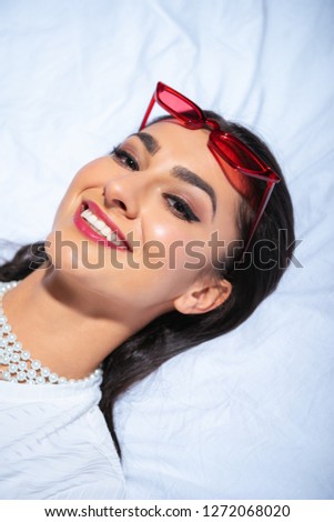 beautiful elegant girl with red eyeglasses on head lying on bed and smiling at camera