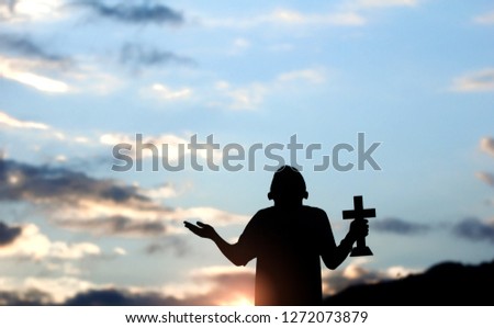 Boy holding christian cross and praying to God with light sunset background,christian concept.