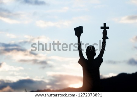 Boy holding christian cross and bible with light sunset background,christian concept.