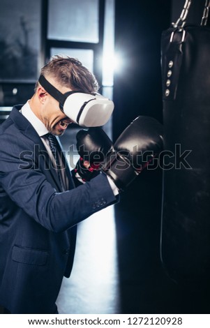 businessman in suit and virtual reality headset boxing and screaming in gym