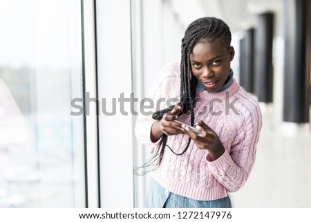 Young afro american woman play games in mobile phone in front of panoramic windows