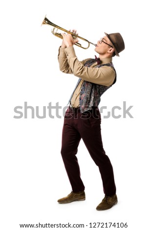 mixed race young man in hat and eyeglasses playing on trumpet isolated on white 