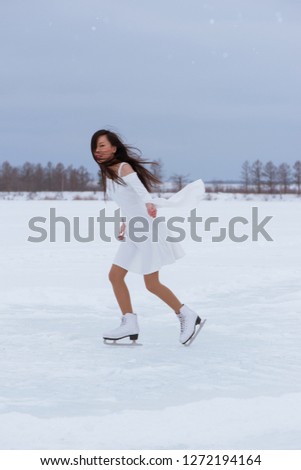 Pretty young woman on skates in white dress at winter frozen park outdoors