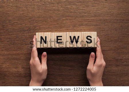 cropped image of journalist holding wooden cubes with word news at wooden table