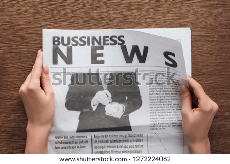 cropped image of journalist reading business newspaper at wooden table
