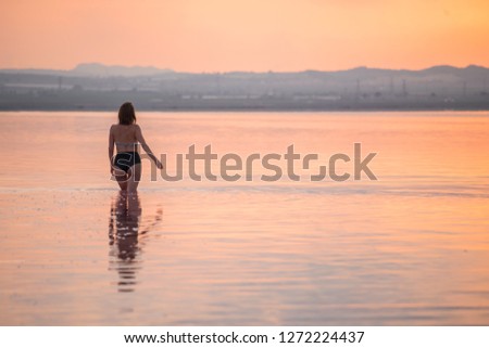 Girl walking on water at sunset. Rear view. Summer happy lifestyle.