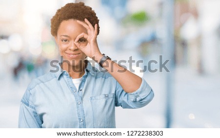 Young beautiful african american woman over isolated background doing ok gesture with hand smiling, eye looking through fingers with happy face.