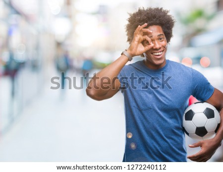 Afro american man holding football ball over isolated background with happy face smiling doing ok sign with hand on eye looking through fingers