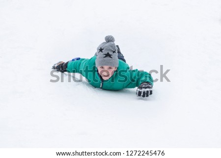 Laughing boy rides on his stomach from a hill. Seasonal concept. Winter day.