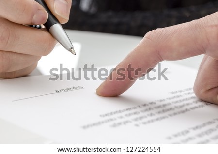 Detail of a woman signing a paper. Male finger showing where to sign.