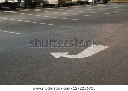 Closeup of white arrow on asphalt ground of the parking lot after raining in the evening. The traffic sign show the symbol of safty and right direction to the goal.