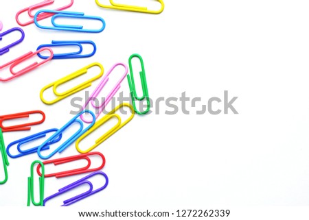 Various colored paper clips lie across a white surface - a background consisting of a white base and colorful paperclips