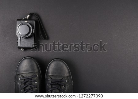 Men's black leather shoes and a black camera on a black background. Copy space.