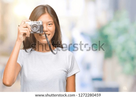 Young asian woman holding vintagera photo camera over isolated background with a happy face standing and smiling with a confident smile showing teeth