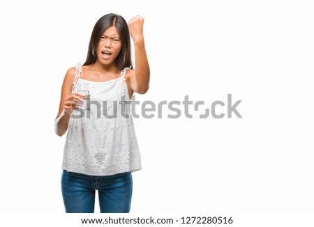 Young asian woman drinking glass of water over isolated background annoyed and frustrated shouting with anger, crazy and yelling with raised hand, anger concept