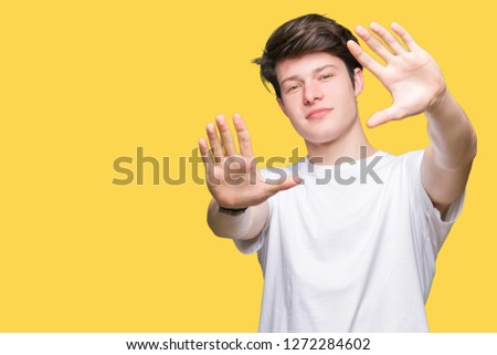 Young handsome man wearing casual white t-shirt over isolated background Smiling doing frame using hands palms and fingers, camera perspective