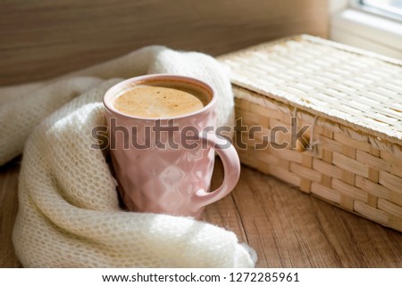 A Cup of hot cappuccino coffee with wicker basket and warm scarf a on wooden table.  Winter mood concept. Autumn mood concept. Warm autumn or winter picture. Selective focus. At home. Time for relax.