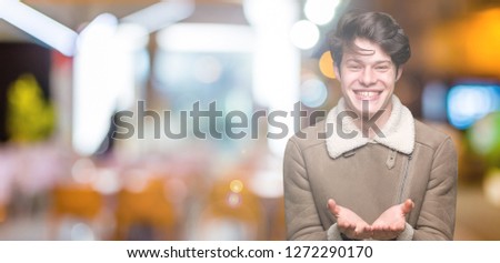 Young handsome man wearing winter coat over isolated background Smiling with hands palms together receiving or giving gesture. Hold and protection