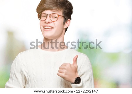 Young handsome man wearing glasses over isolated background doing happy thumbs up gesture with hand. Approving expression looking at the camera showing success.