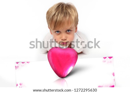 Pink box in a shape of heart with a metallic texture on a white background with heart decor in front and behind there is a child boy lying on the floor