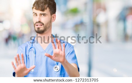 Young handsome nurse man wearing surgeon uniform over isolated background afraid and terrified with fear expression stop gesture with hands, shouting in shock. Panic concept.