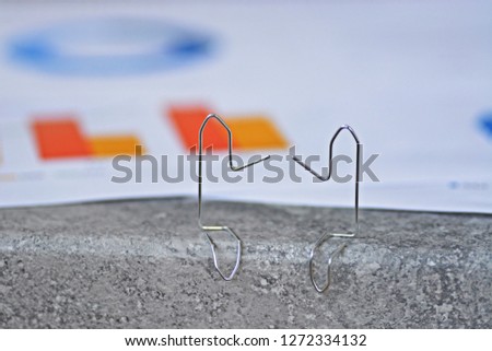 Two paperclips bent to small male sit on a surface and have statistical evaluations and diagrams behind them - Abstract concept for representing business discussions