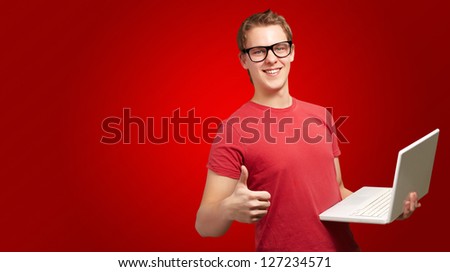 Man holding laptop with thumbs up isolated on red background