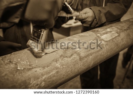 Restoration of the strength characteristics of the industrial pipeline. Resin coating on pipe. Hands and spatulas. Picture taken in Ukraine, Kiev region. Black and white image. Sepia