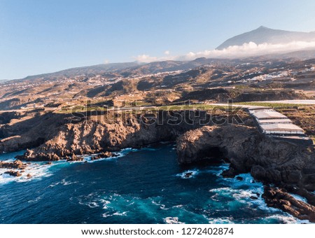 Cliff of volcano stones in the north of Tenerife with El Teide on the Top with clouds. Ocean and banana trees. Aerial picture with a drone