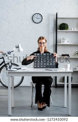 attractive businesswoman in black clothes and glasses showing calendar 