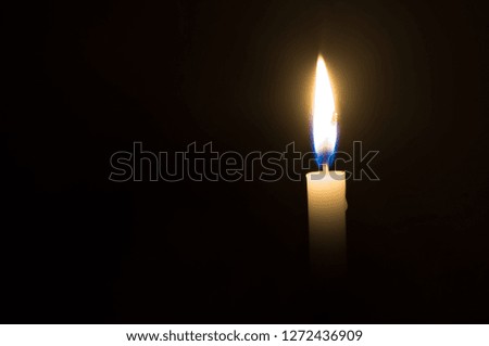 A single candle light glowing on a white candle on black background, a single candle light glowing in a dark room